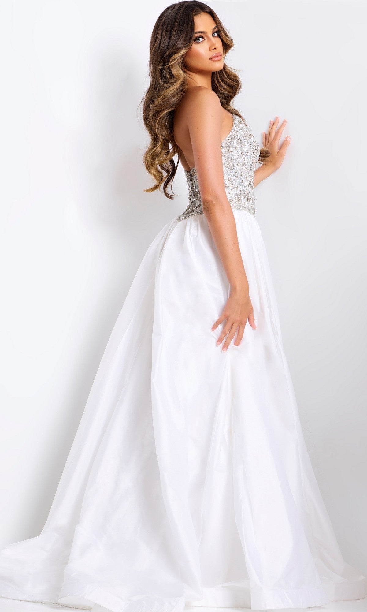 A woman wears the Long Prom Dress: Jovani 49247—a white strapless ball gown with an embellished bodice and flowing satin a-line skirt—standing against a plain white background, looking over her shoulder.